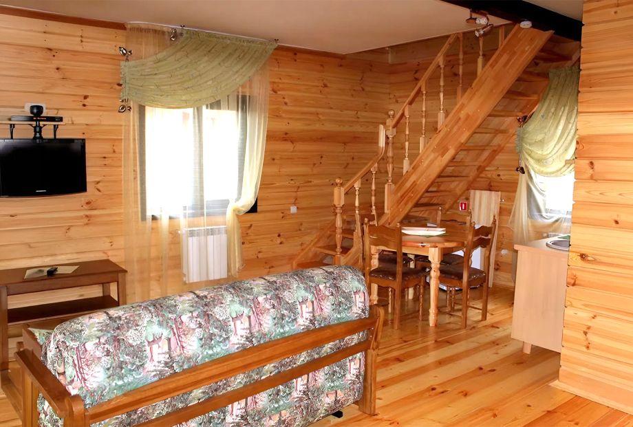 Коттедж на 12 человек на базе отдыха «Аркадия»: гостиная с диваном и окном на сосновый бор